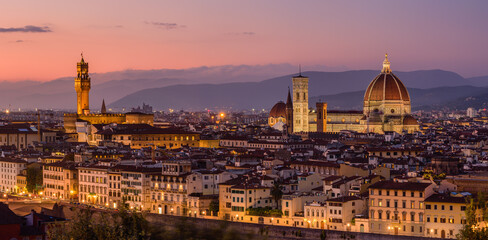 The illuminated Florence cityscape with the Palazzo Vecchio and the Florence Cathedral in an orange and purple twilight.