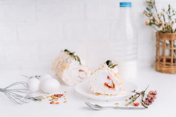 Meringue roll without sugar on a white plate cut into pieces in front of a bottle of milk and eggs.