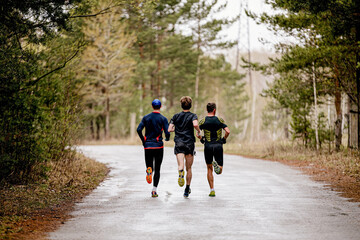 back three male athletes run race on road in park