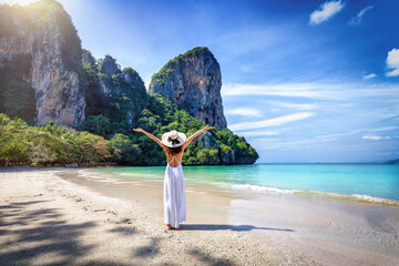 A happy tourist woman in a white dress and stands on the beautiful beach of Railay at the Krabi...