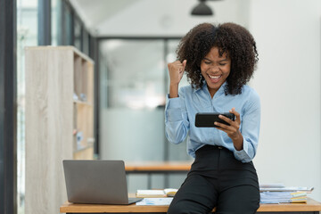 Young african american businesswoman sitting on the desk at the office while making a video call with a business colleague in receiving good news on modern business contracts.