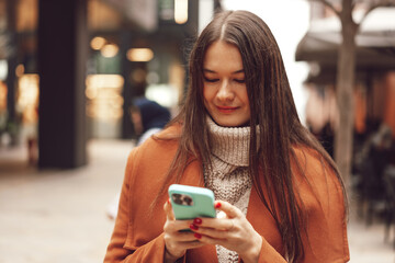 Young woman in brown coat using the phone on the city streets