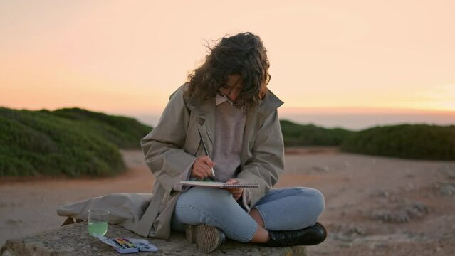 Creative girl drawing sketch at evening ocean mountain. Focused woman painting