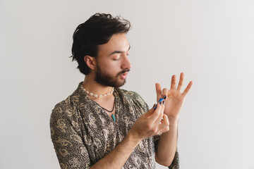 Young queer latin gay man showing how he paints his nails on camera on a white background.