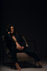 Fototapeta na wymiar Beautiful pregnant girl at the studio. A pregnant girl in a man's suit.Stunning pregnant woman - maternity photography of a beautiful young expecting mother to be on a black background, studio photogr