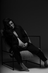 Obraz na płótnie Canvas Beautiful pregnant girl at the studio. A pregnant girl in a man's suit.Stunning pregnant woman - maternity photography of a beautiful young expecting mother to be on a black background, studio photogr