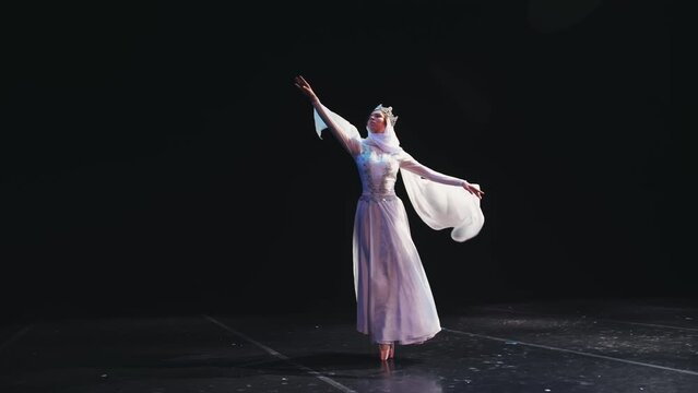 A ballerina in a beautiful white suit and a crown stands beautifully on the stage of the theater. The wind blows her clothes. The concept of freedom, determination.