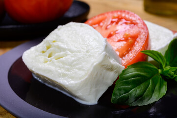 Sliced white ball of Italian soft cheese Mozzarella di Bufala Campana served with fresh green basil and red tomato