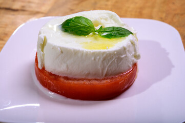 Sliced white ball of Italian soft cheese Mozzarella di Bufala Campana served with fresh green basil and red tomato
