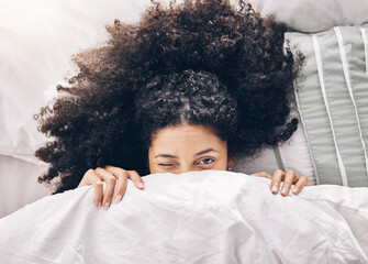Bed, wink portrait and black woman in the morning after sleep and rest at home with blanket. Eyes, house and wake up happiness of a young person hiding face under the bedroom covers on a pillow