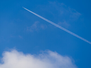 The plane leaves a white trail over white cloud in blue sky