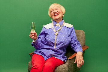 Happy old woman, grandmother in stylish colorful clothes sitting with legs into bowl and drinking...