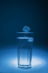 natural mineral healthy water in a transparent glass and drops of water splash out of the glass on a blue background. for signage banners labels postcards advertising