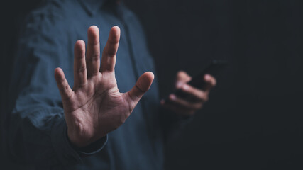 Man hand showing stop gesture with hand holding smartphone, close up of the hand with gray background and copy space for text. stop and solve  problem concept.