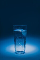 natural mineral healthy water in a transparent glass and drops of water splash out of the glass on a blue background. for signage banners labels postcards advertising