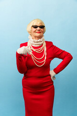 Lady. Beautiful old woman, grandmother in stylish red dress, sunglasses and pearl necklace posing...