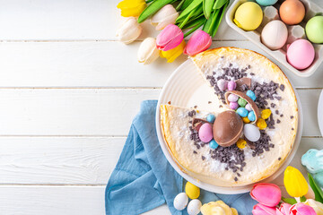 Homemade Easter cheesecake, sweet cottage cheese baking, with Easter chocolate eggs and chocolate drops, with holiday decorations and spring flowers