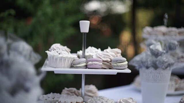 The festive table is covered with a colorful white tablecloth, decorated with capcakes and macaroons in three tiers. Celebration of the wedding concept. Luxury candy bar on white wedding