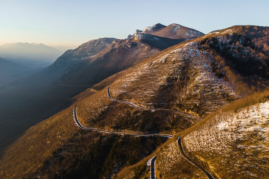Aerial view of a scenic forest road on mountainside in wintertime at sunset with snow on Mount Terminio, Serino, Avellino, Irpinia, Campania, Italy.