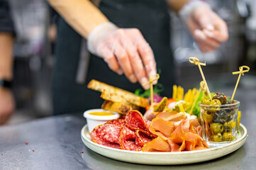 woman chef cooking Antipasto plate with ham, prosciutto, salami, cheese, vegetables and olives on kitchen