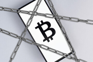 Fototapeta na wymiar Bitcoin and blocking, cancellation, ban, crisis concept. Cryptocurrency symbol Bitcoin on screen of mobile phone and steel chains, symbol of prohibition, cancellation. Astana, Kazakhstan 14.02.2023