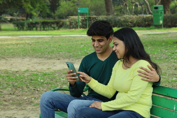 Young Indian Happy couple sitting on a park bench in a serene atmosphere playing with a paper...