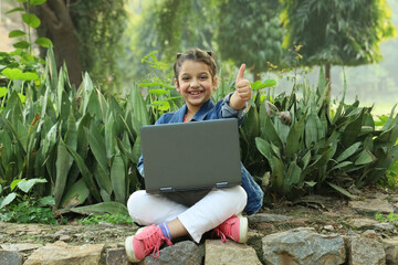 Happy Indian girl working on a Laptop in a lush green park in day time in summer. Busy with work he...