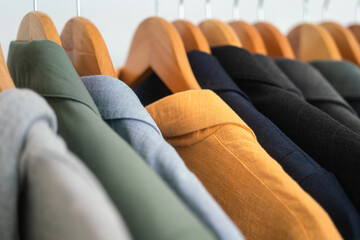 Row of colorful cotton coat suits are hanged by wooden cloth hanger on the rail. Fashion lifestyle object, close-up and selective focus.	
