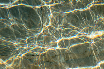 Colorful sun glare on the water in the fountain with an old stone floor, unusual abstract texture