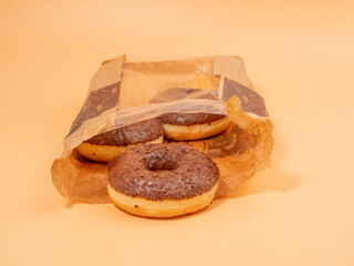 Chocolate donut with chocolate chips in a paper bag on an orange background. close-up.