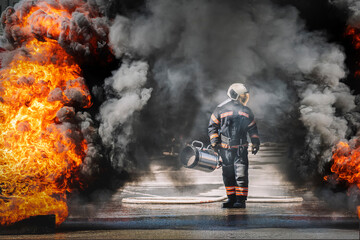 hero firefighter with a hose looks at the strong flames from the fire and black smoke. Heroic dangerous work of firefighters