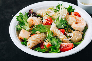 Seafood salad bowl. Green lettuce tomato salad with shrimps, scallop and squids