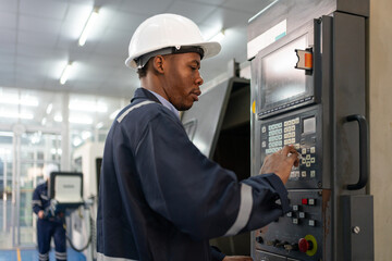 Male engineer operating cnc machine in control panel at factory. Man technician in uniform and helmet safety working at workshop heavy metal industrial