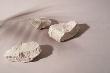 Abstract minimalistic scene with shadow of a palm leaf , stones. Podium on a light background with shadows. product presentation, layout, demonstration of a cosmetic product, podium, stage pedestal or