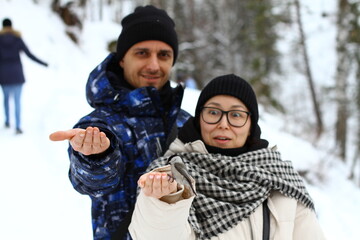 Young couple feeds birds on the winter forest. Small titmouse bird in people's hand. Snow background.