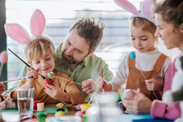 Happy family with little kids decorating easter eggs.