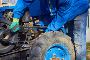 a man repairs a tractor,the mechanic repairs the walk-behind tractor, replacing the drive belt of the walk-behind tractor