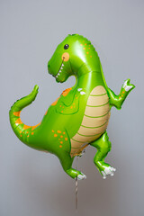 Fototapeta premium green dinosaur, foil balloon green dinosaur with latex balloons on the background of the wall, postcard with a dinosaur