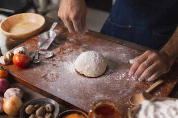 Close-up of a human hands kneading dough to make homemade pizza. Apron and hands knead the dough. Making dough by hand in a bakery. Preparing dought for pizza at home