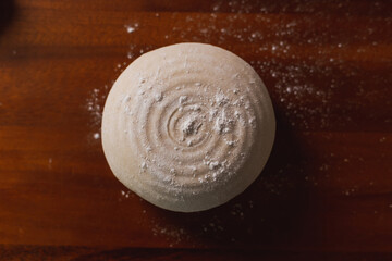 Top view homemade ball of fresh raw dough for pizza or bread baking on wooden board. Pizza dough with flour. Preparation of the dough.
