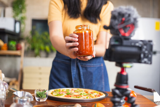 Young attractive Asian woman talking communicating during online live streaming how to cook homemade pizza indoor kitchen. content creator using camera recording food product review.