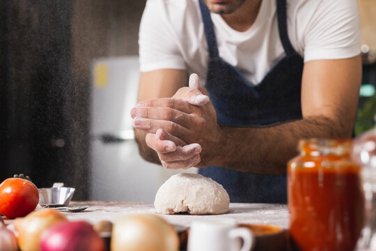 Close-up of a human hands kneading dough to make homemade pizza. Apron and hands knead the dough. Making dough by hand in a bakery. Preparing dought for pizza at home