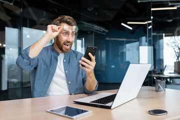 Mature man shocked by bad news and online notification received on phone, businessman at work...