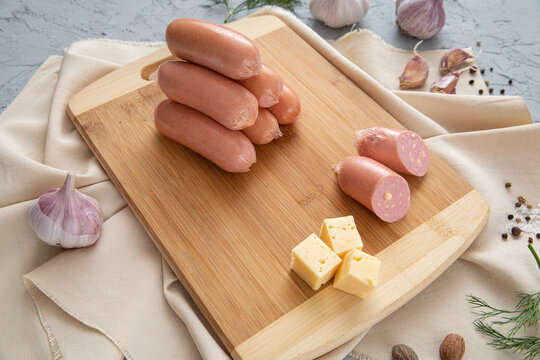 Cheesy sausages with cheese, garlic, spices and greens on wooden cutting board on textured gray background. Copy space. For design.