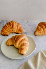 três croissant em fundo claro e prato de porcelana branco com espaço para texto