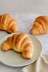 três croissant em fundo claro e prato de porcelana branco