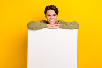 Photo of positive successful man wear khaki clothes stand behind board empty space promote store isolated on yellow color background