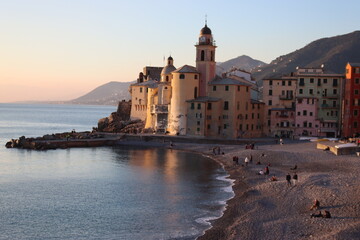 Fototapeta premium Camogli, Italy - January 27, 2023: Beautiful old mediterranean town at the sunrise time with illumination during winter days. People enjoying the evening at the beach with beautiful sunset background