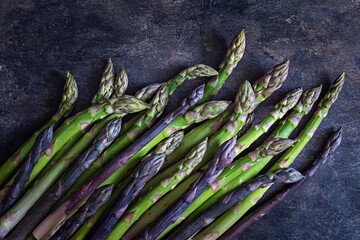 Purple, green asparagus on a dark background. Raw food concept. The vegetable is rich in fiber, natural prebiotic, low key.