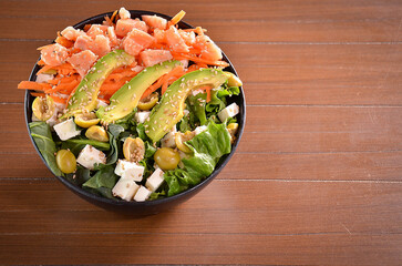A bowl with vegetables, tomatoes, avocado, and cheese